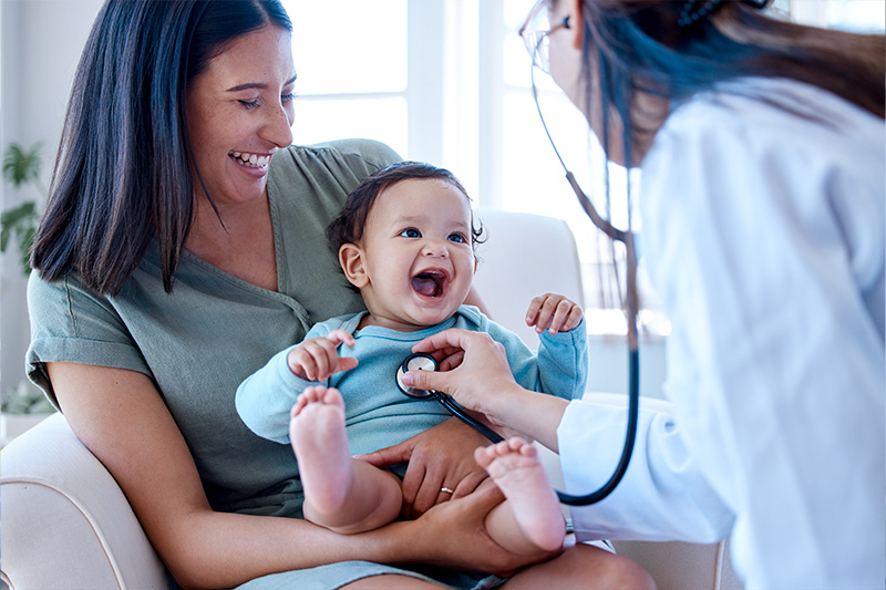Woman holding baby who is being tended to by a doctor.