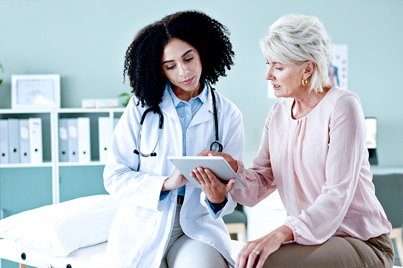 Cardiology specialist speaking with an eldery female patient, while looking at a tablet with test results.